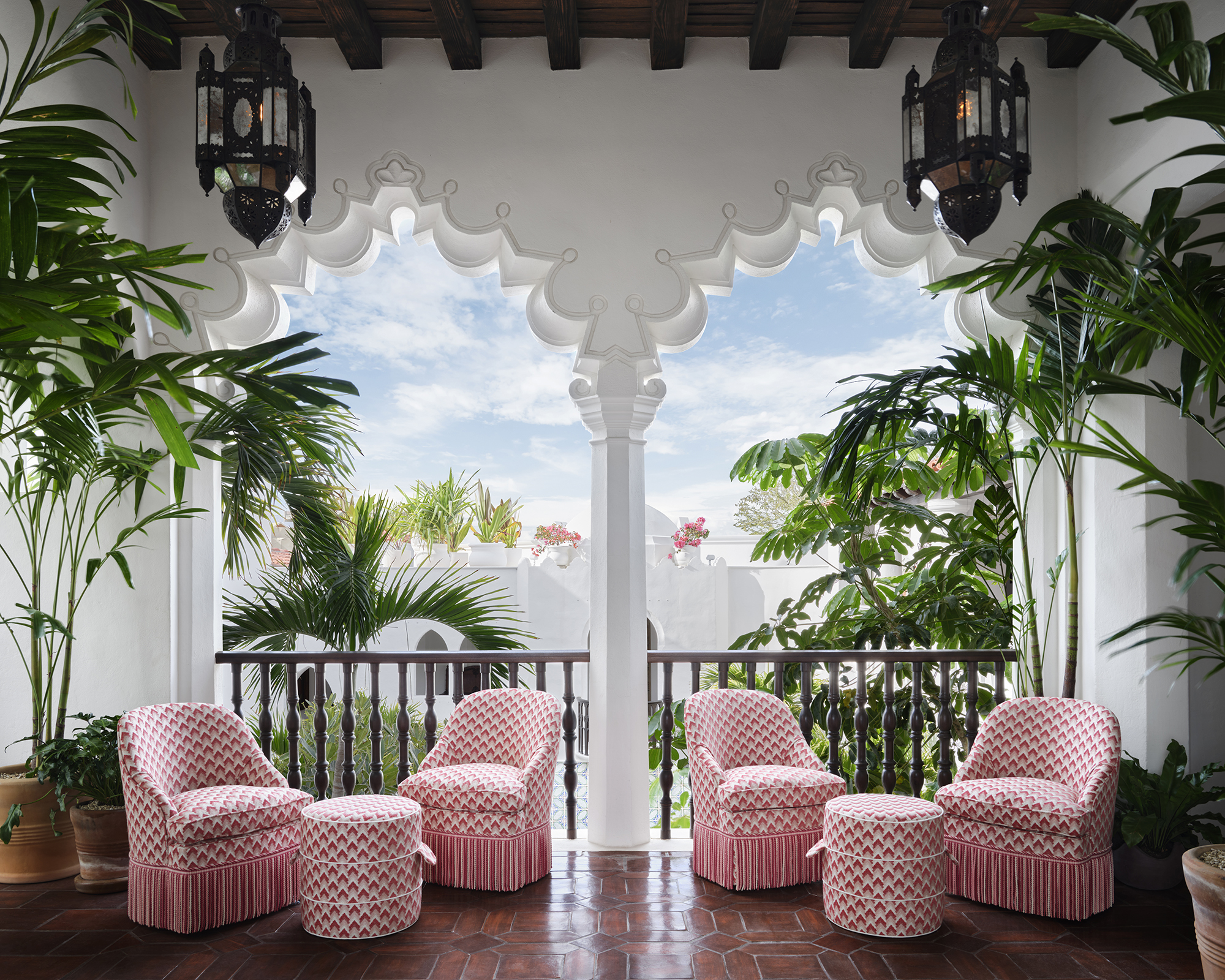 sun terrace with pink check arm chairs and matching pink check coffee tables looking out to palm trees