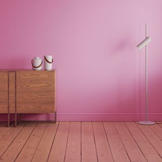a wooden sideboard and white floor lamp in front of a pink wall, with wooden slat floorboards