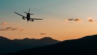 A plane flying over a mountain at sunset