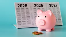A piggy bank standing in front of a calendar for 2025-2027 and a pile of coins on a light blue background