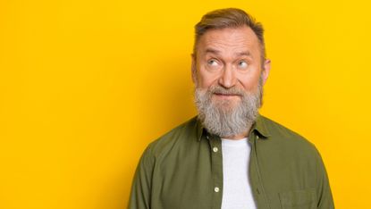 Portrait of thoughtful bearded mature man against a bright yellow background
