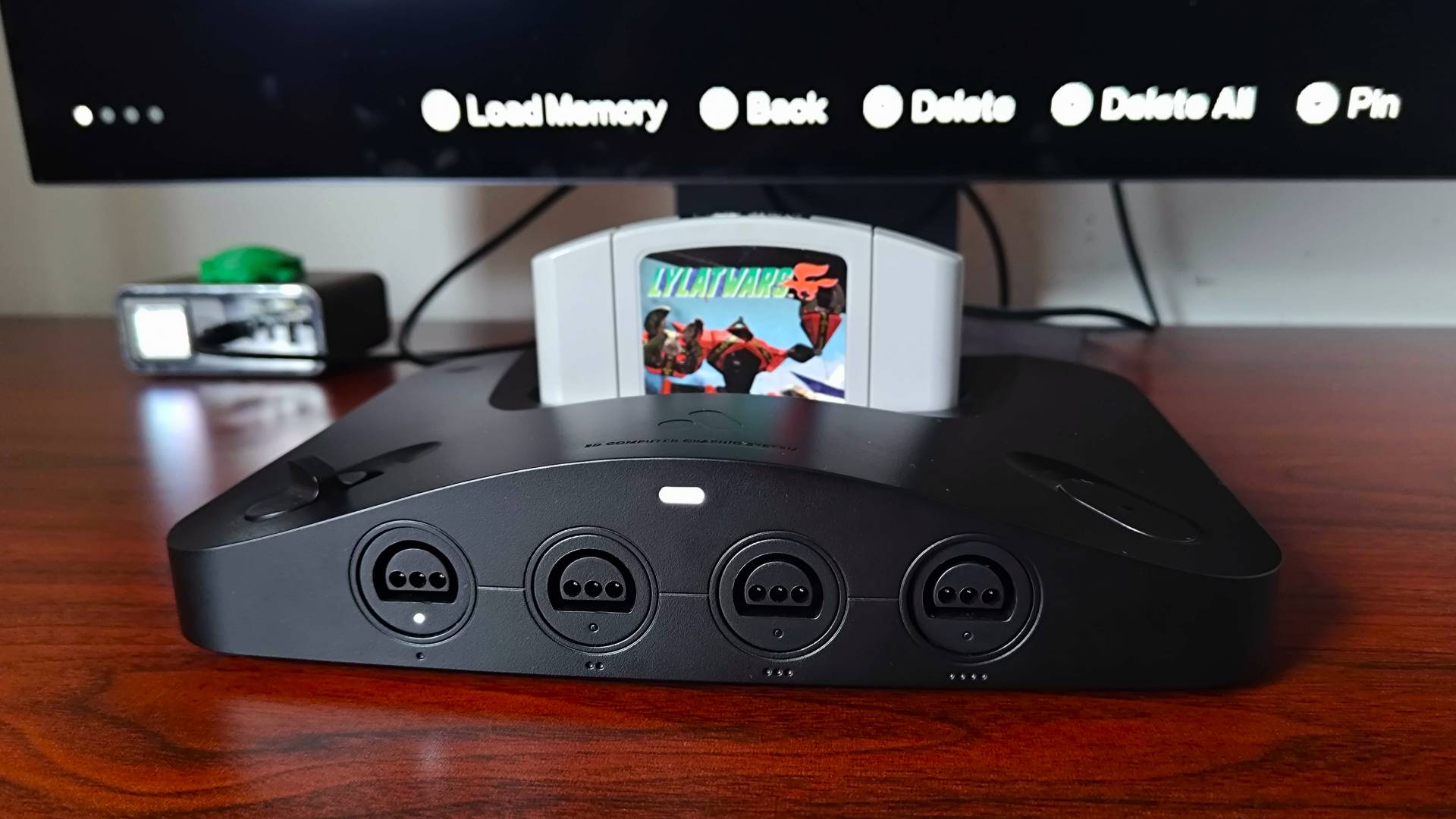 Close up of Analogue 3D on woodgrain desk with Star Fox 64 (Lylat Wars) cartridge inserted and monitor in backdrop with new Memories save states feature active.