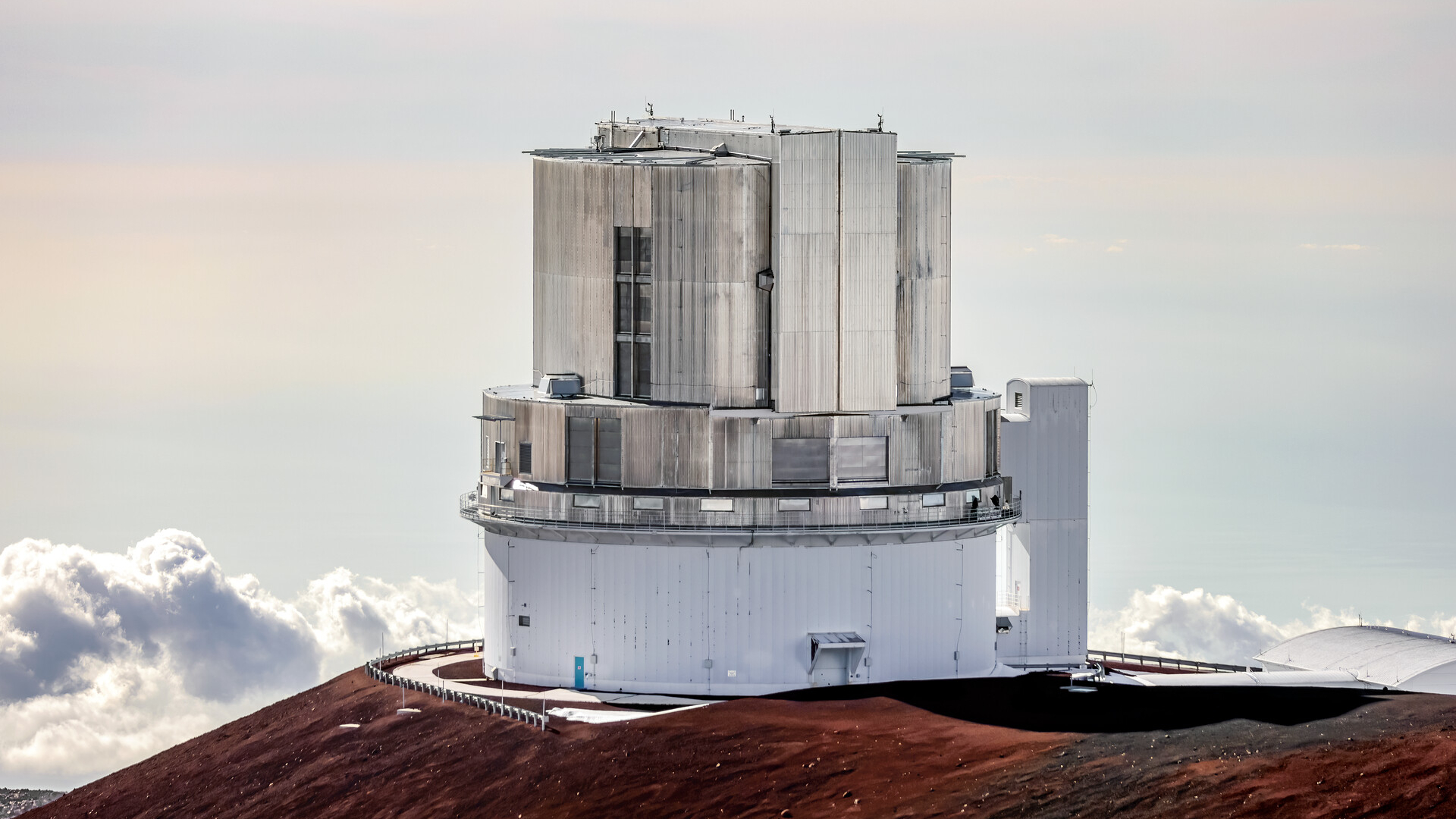 Un gran edificio redondo de metal se asienta sobre un acantilado con nubes en la distancia