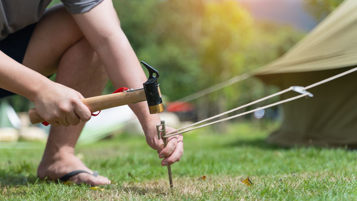 Closeup man hitting a metal tent peg by a hammer into the ground 