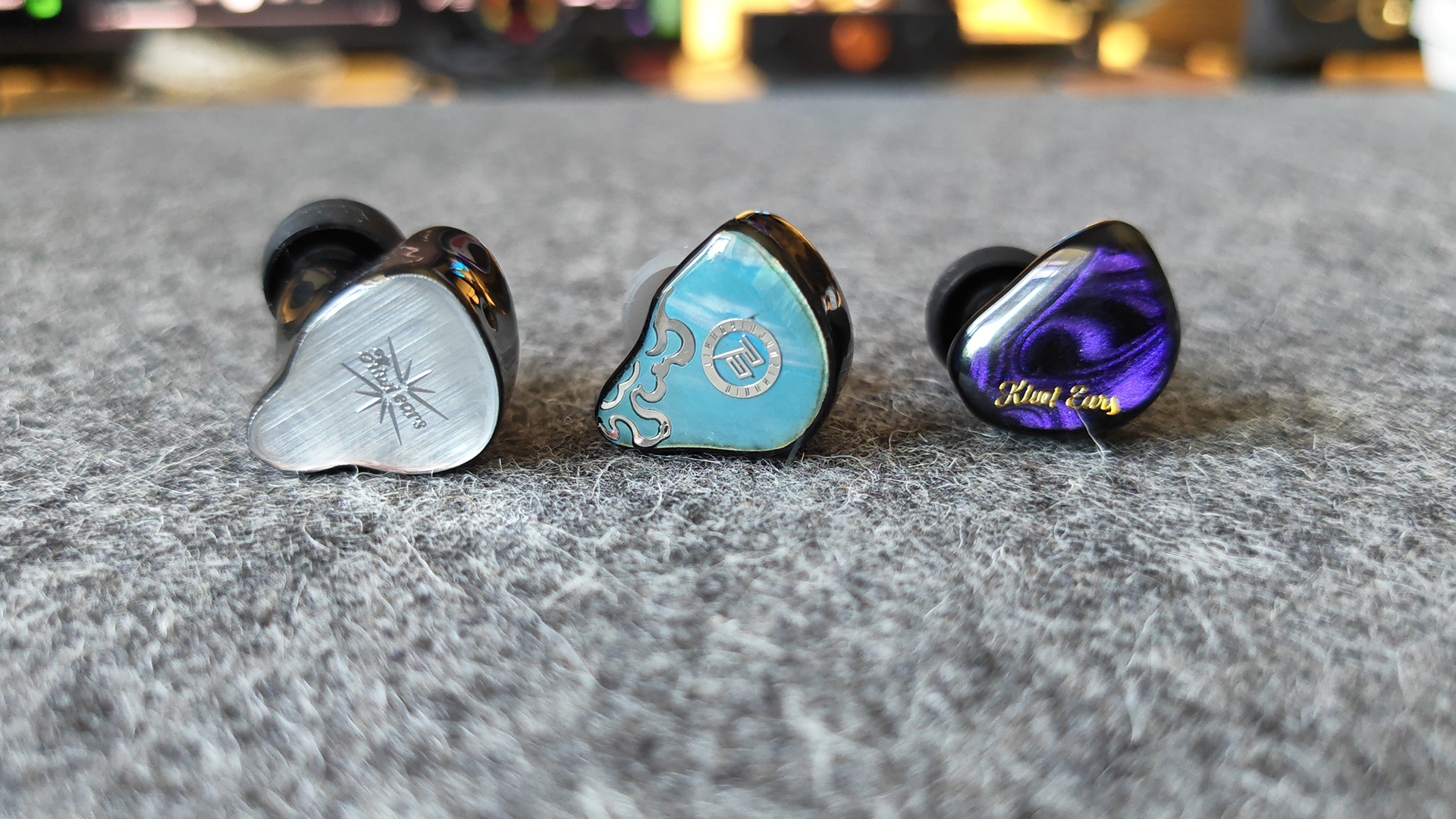 Three IEMs on a felt desktop mat.