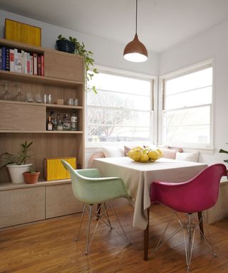 A dining nook with bright chairs and a built-in wooden shelving system with cookbooks and kitchen essentials