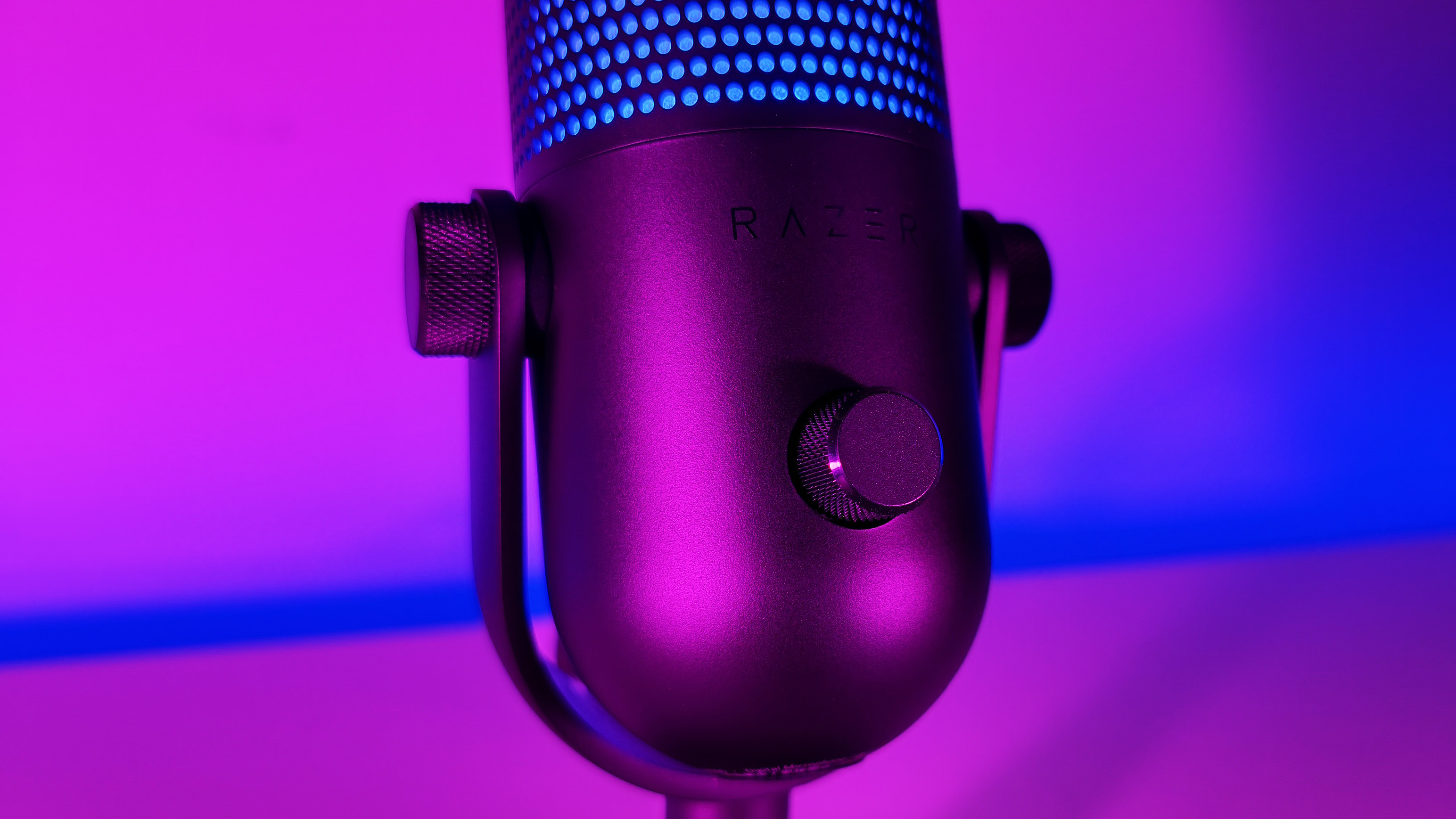 Close-up view of the front control knob and Razer logo on the Seiren V3 Chroma microphone, illuminated by neon pink and blue lighting.