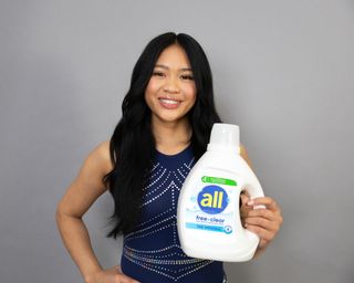 suni lee on a gray background holding all free clear detergent