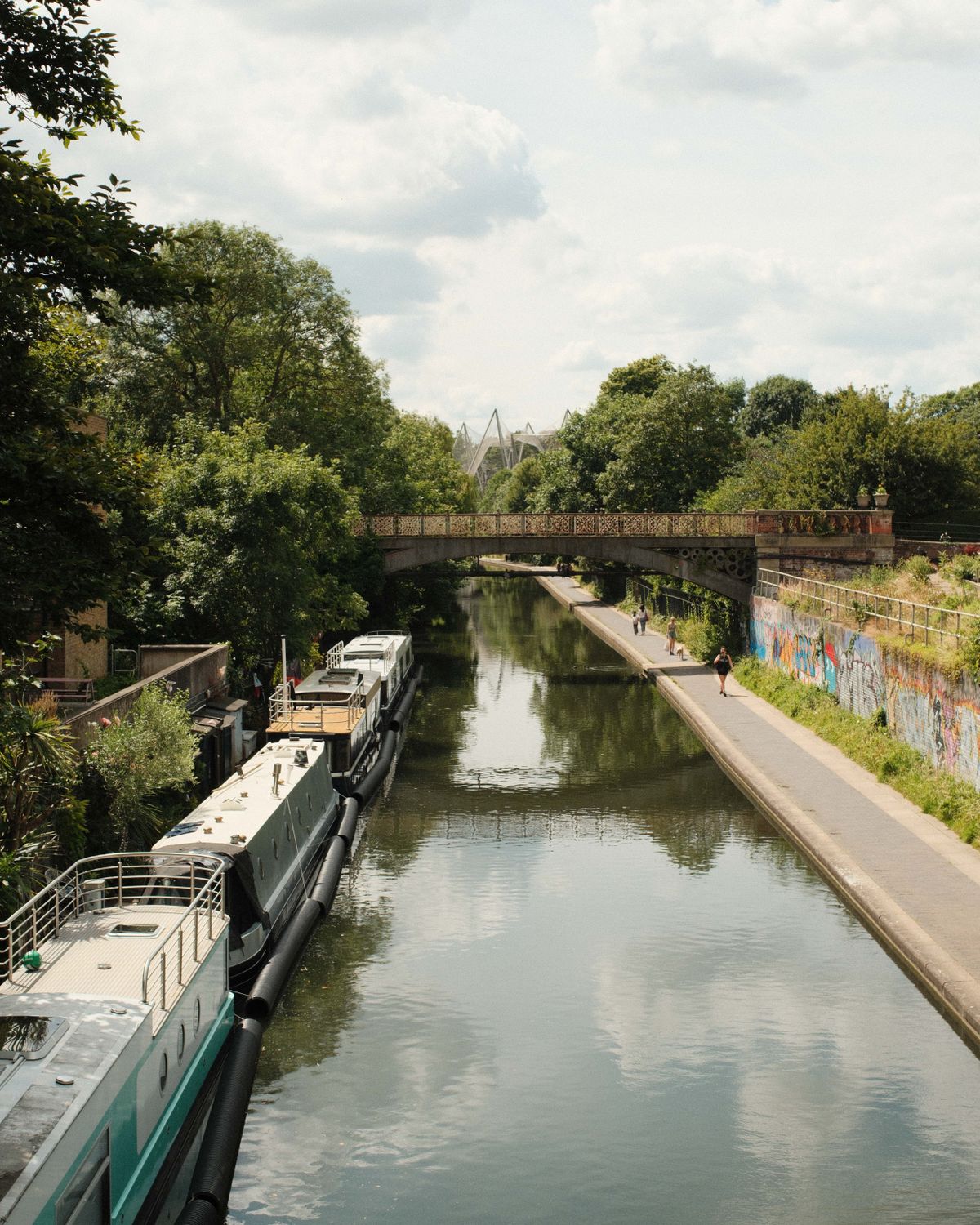 Boats sailing up a canal with next to a tow path with people walking