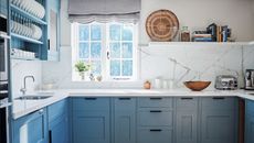 Kitchen with pale blue fitted cabinets, white worktop and walls and tiled floor. 