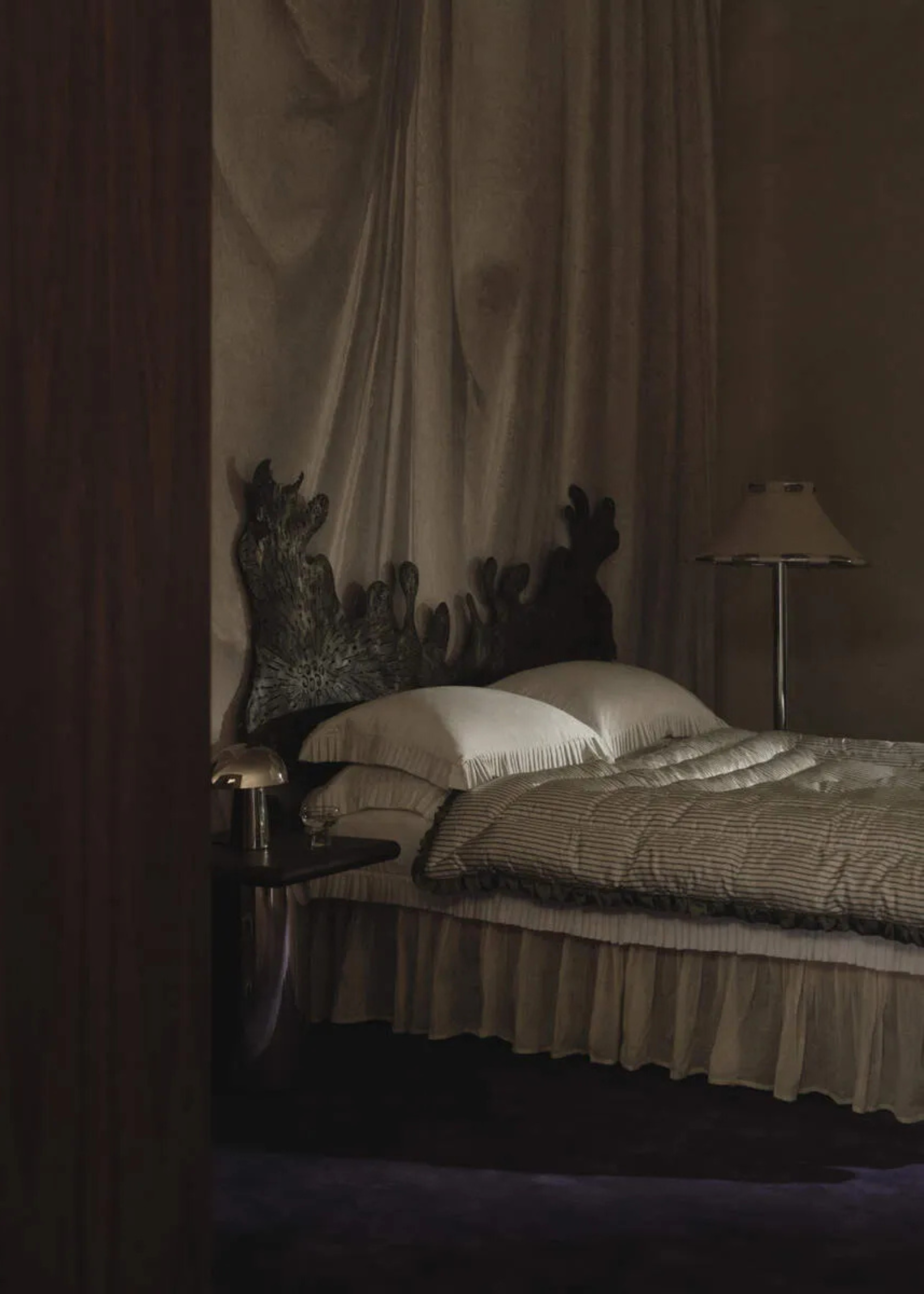 A gothic romance bedroom with a textured headboard, chrome lamps, and a draped backdrop