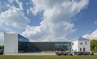 Daytime, exterior view of the Cacao Factory, Helmond, white and glass fronted building, grass lawn, trees, pathway, parked cars, blue cloudy sky