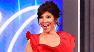 Julie Chen Moonves smiling ear to ear on the Big Brother stage in a red dress