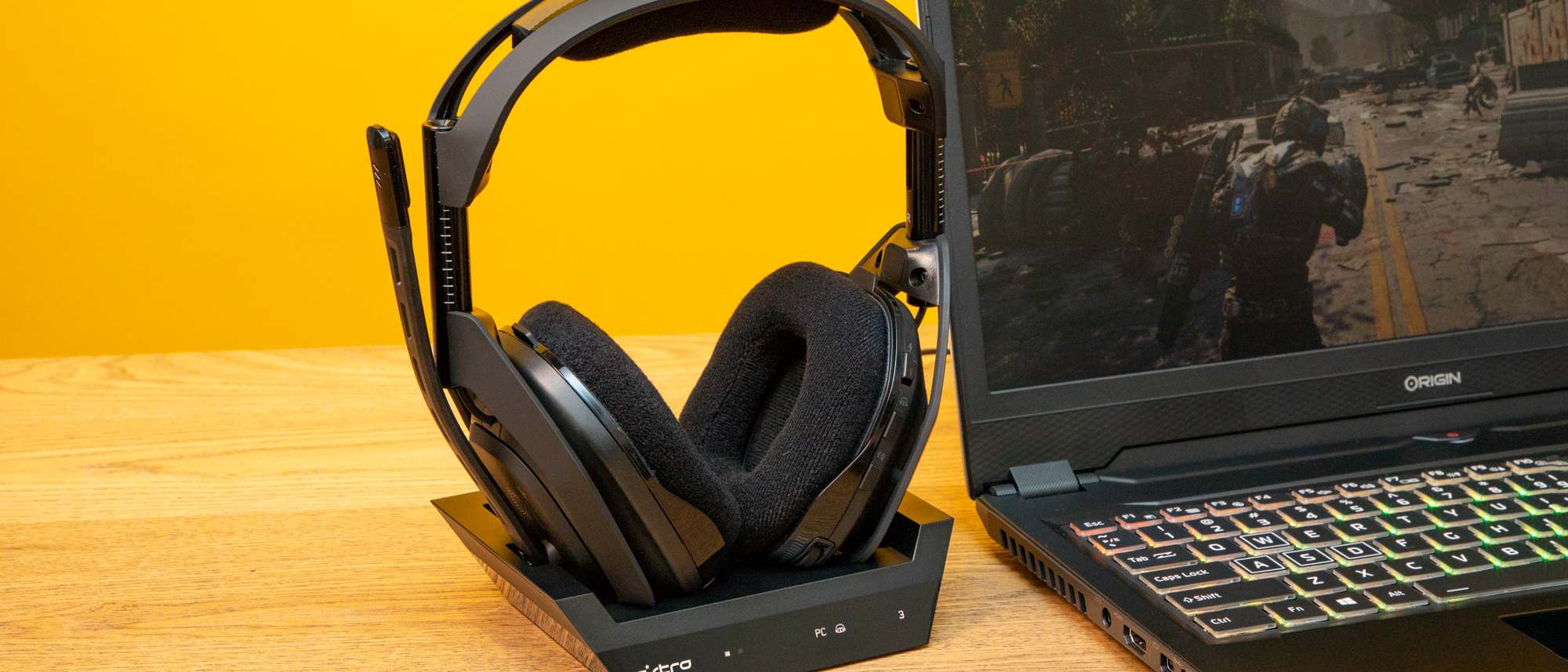 Gaming-headsettet Astro A50 i svart står på et skrivebord, ved siden av en åpen laptop.