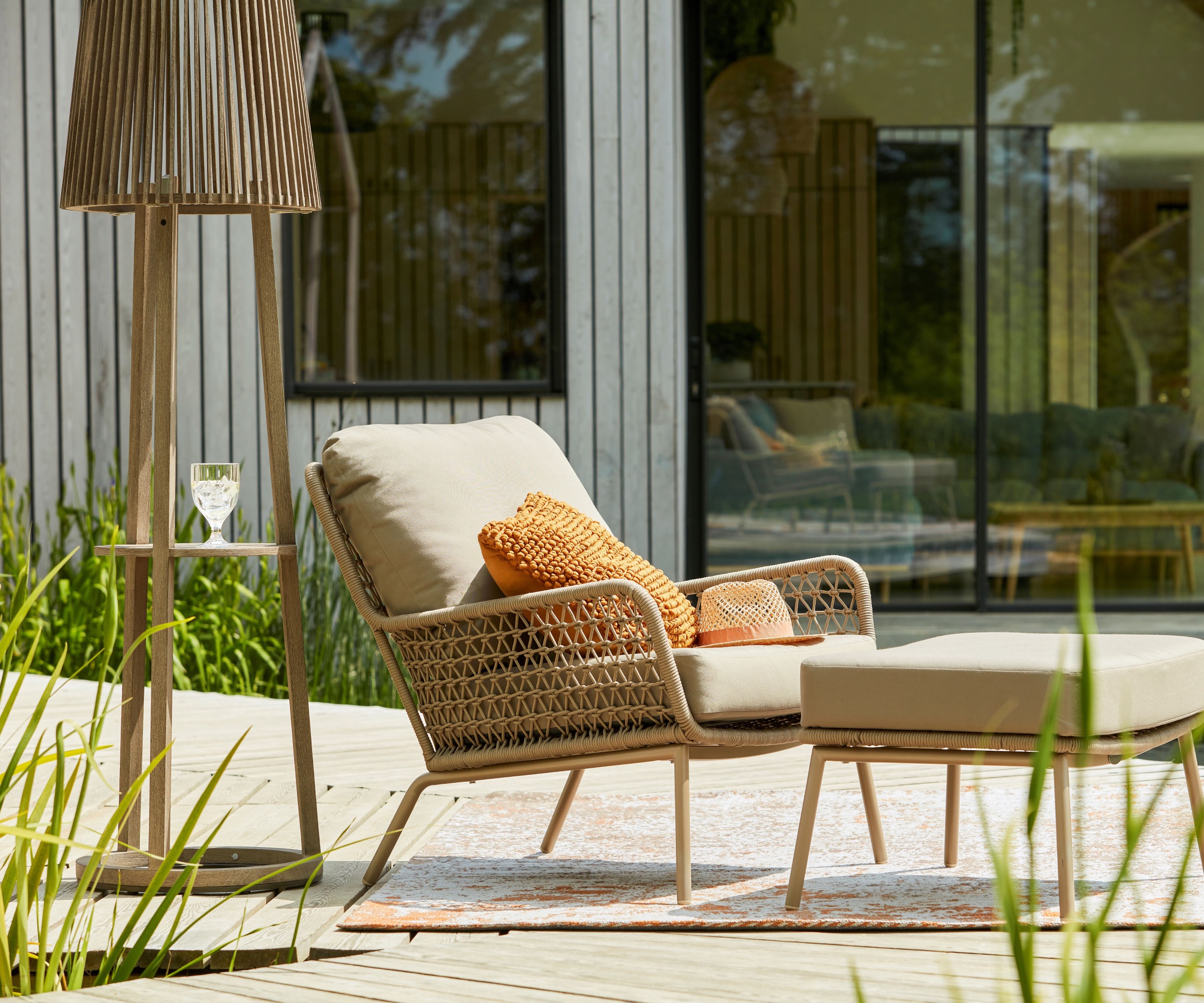 Solar outdoor lamp next to woven armchair and stool on decking