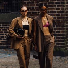 two attendees at Copenhagen spring 2023 fashion week wearing sunglasses, crop tops, and brown suits 