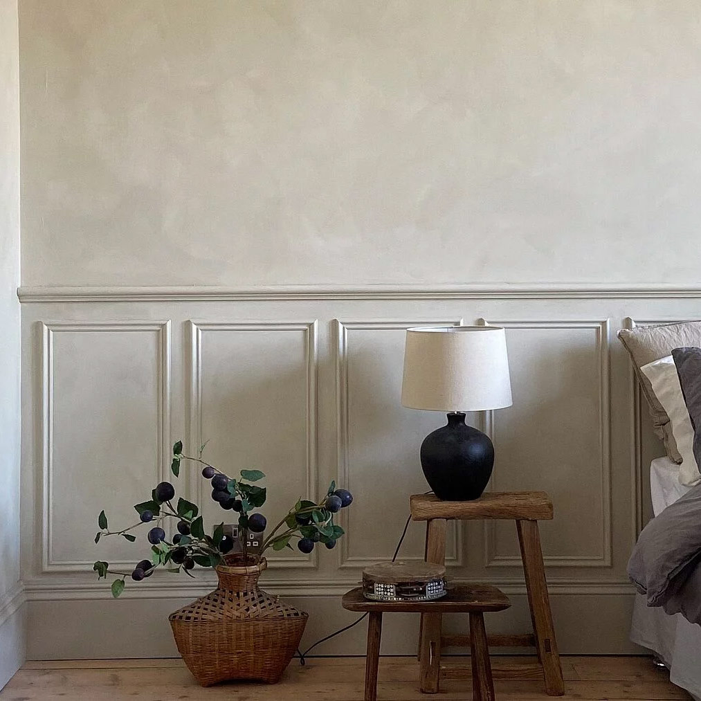 KEIM Colourwash limewash effect paint featured in a bedroom with a planter, set of side tables, and table lamp