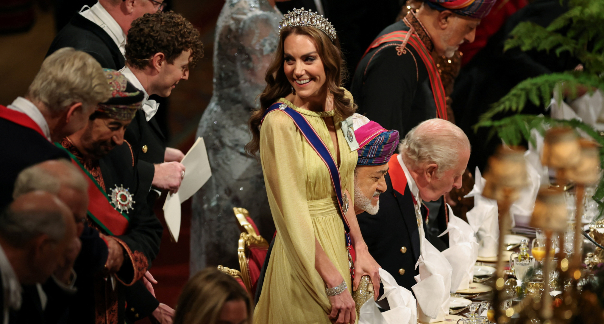 Princess Kate wearing a yellow gown and tiara standing at a table