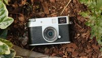 Fujifilm X Half camera on wood chips surrounded by green plants