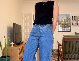 Woman wearing Alex Mill cashmere vest and Still Here jeans inside a mid-century modern living room.