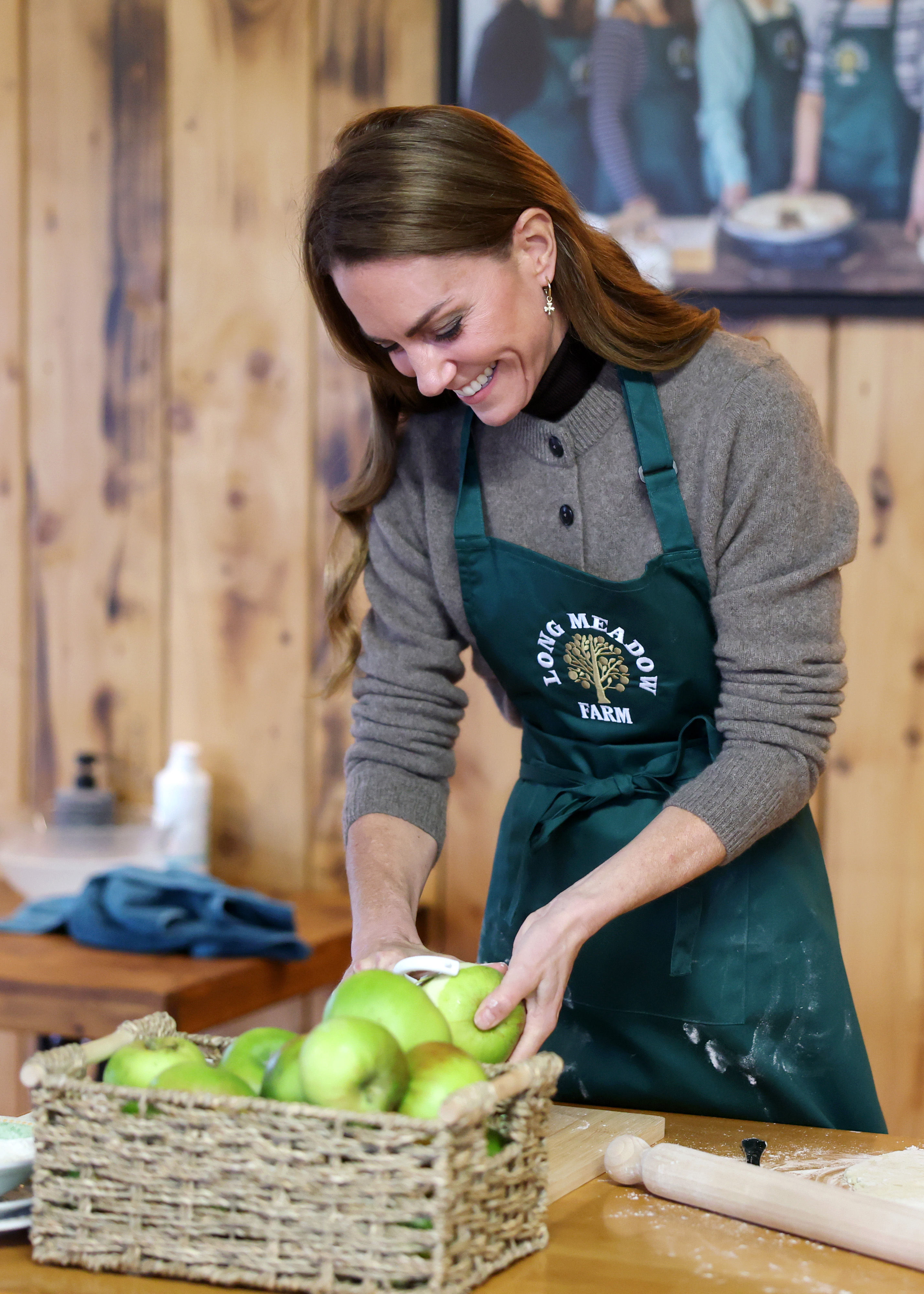 Kate Middleton wearing a brown cardigan and a green apron peeling apples