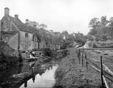 A villager fetches water from the river next to Arlington Row in Bibury, pictured in 1912. ©Country Life Picture Library