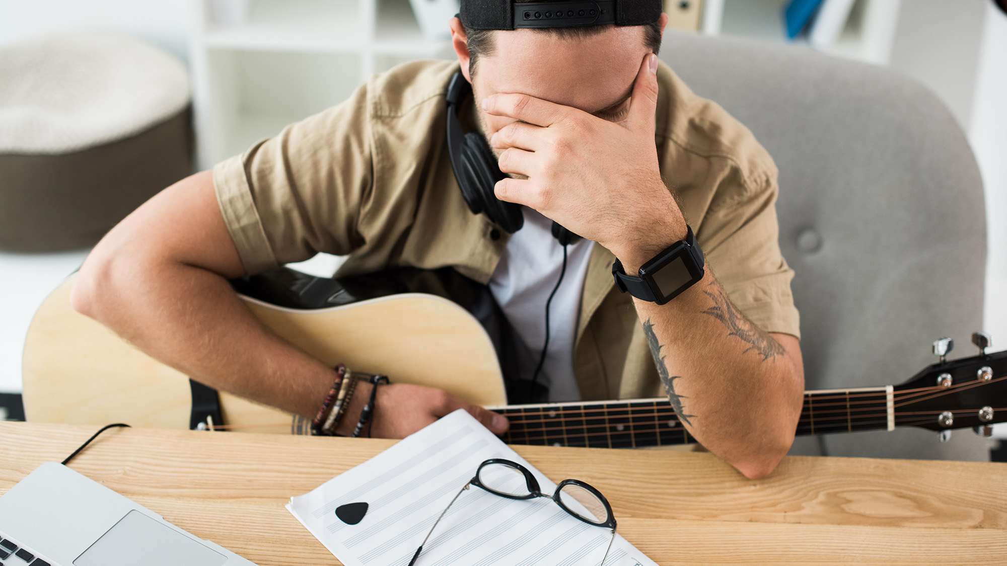 A young man sits at his desk playing electric guitar, a laptop with lesson open in front of him