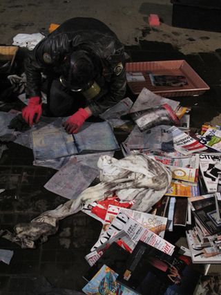 Man wearing gas mask looking through magazines