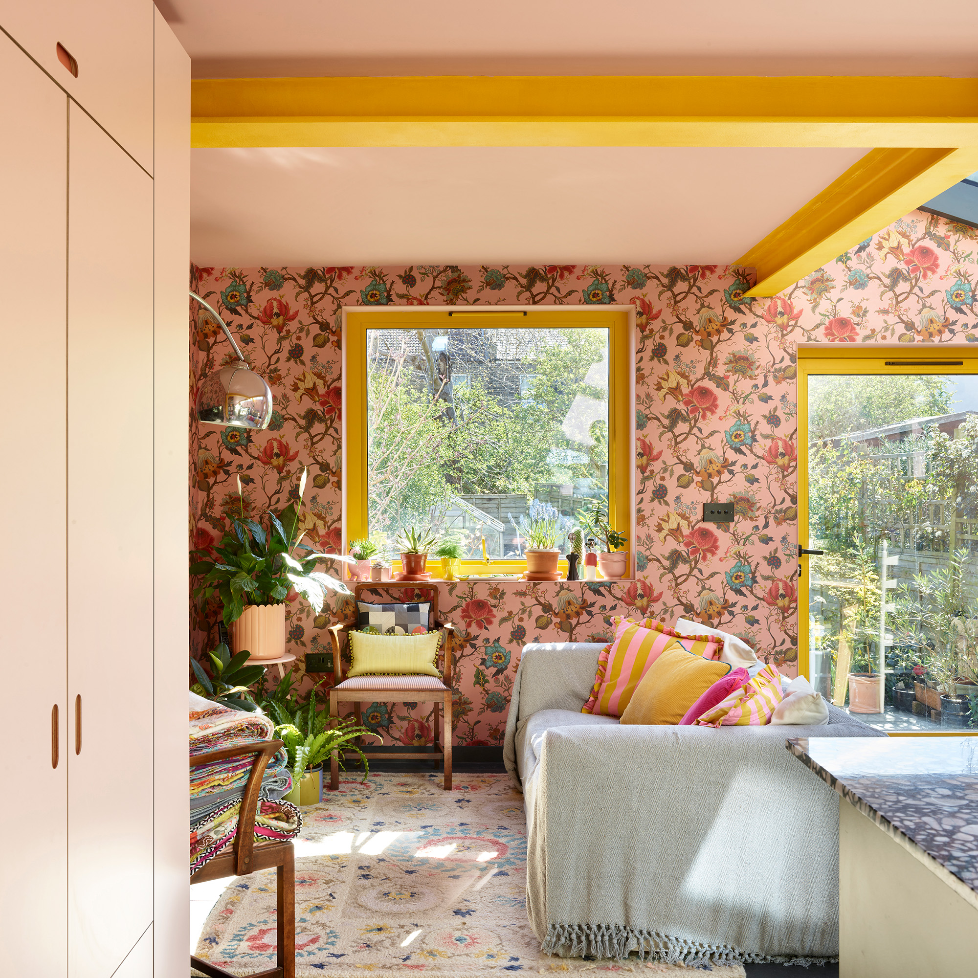 colourful open plan kitchen with cosy seating areas with pink floral wallpaper, pink ceiling yellow steel beams and yellow framed window .jpg
