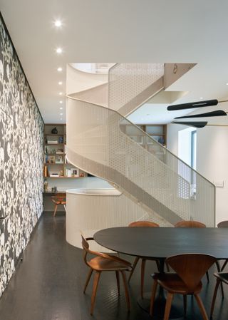 room with patterned wall, dark flooring, dining table and chairs with a central white staircase leading to the floor above