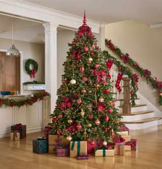 An entryway with wooden flooring, a staircase, and a large Christmas tree with red decorations