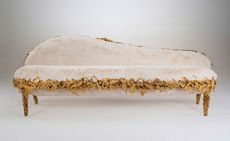 A white furry sofa with a sloped backrest and gold trim.