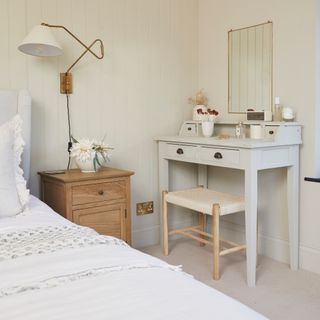 how to decorate a guest bedroom, neutral bedroom with dressing table/desk, brass wall light, white bedding, cream tongue and groove on walls