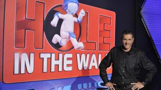 Dale Winton standing in front of the Hole in the Wall show logo
