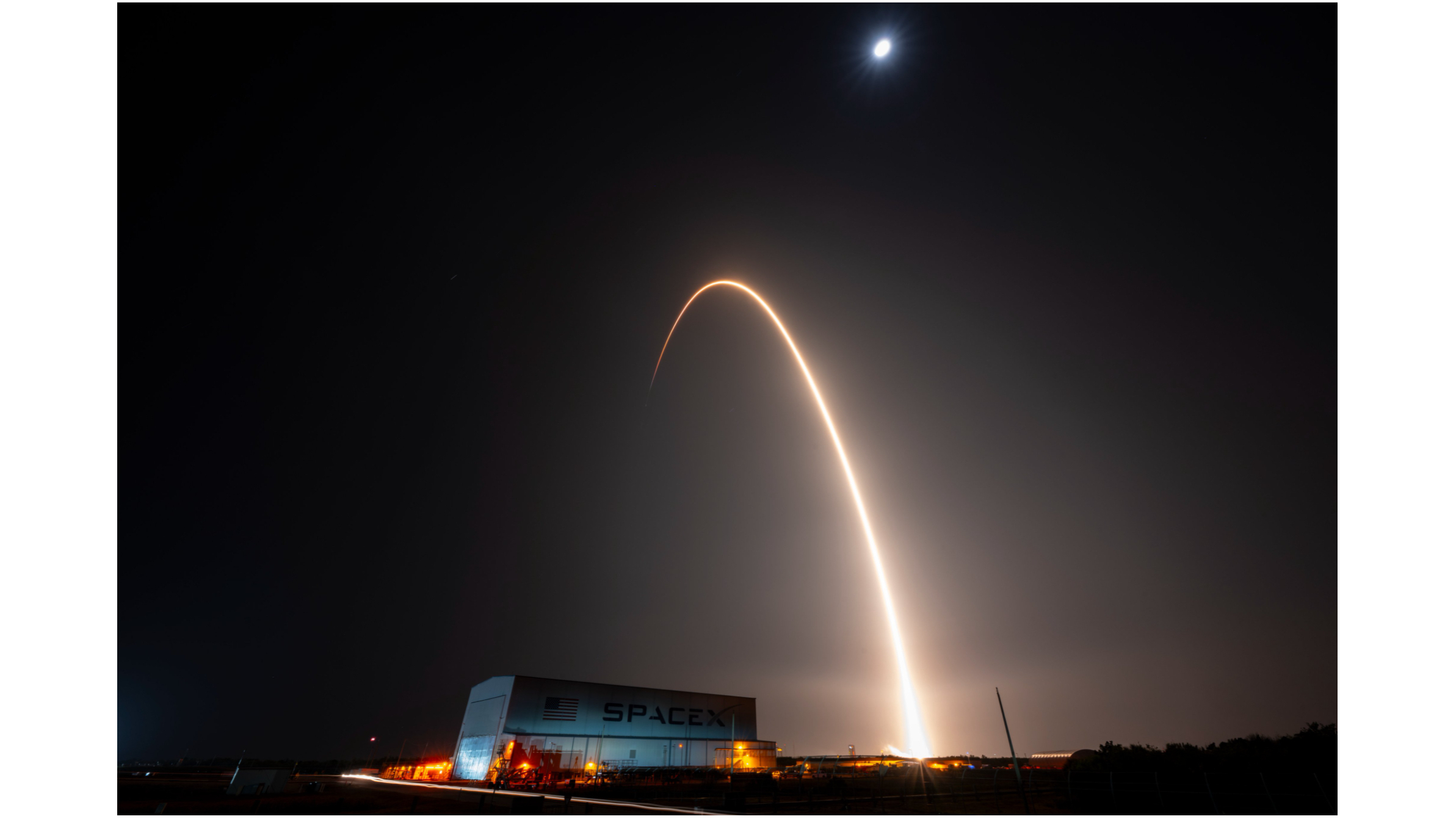 A rocket launch carves an orange arc into a dark night sky in this long-exposure photo.
