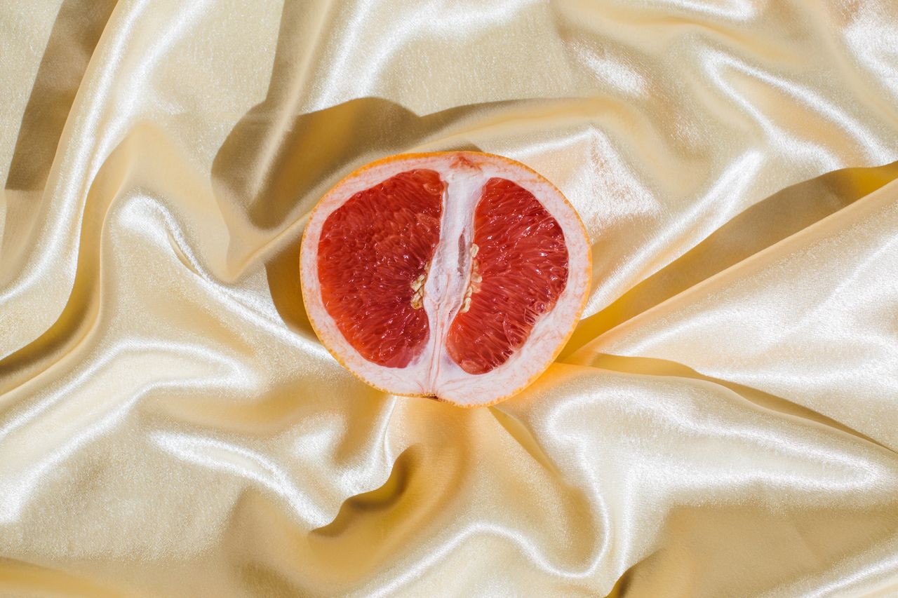 Pelvic floor dysfunction: Fresh grapefruit on beige soft silk fabric background. Sex concept. Women&#039;s health, sexuality, erotic tension. Female vagina and clitoris symbol