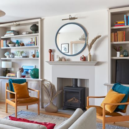 a neutral living room with pops of bright colour, a cream sofa, yellow mid century style armchairs and a round mirror over a fire surround