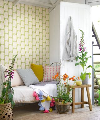 Cozy she shed ideas with white walls and a green and white wallpaper and daybed with colorful pillows.