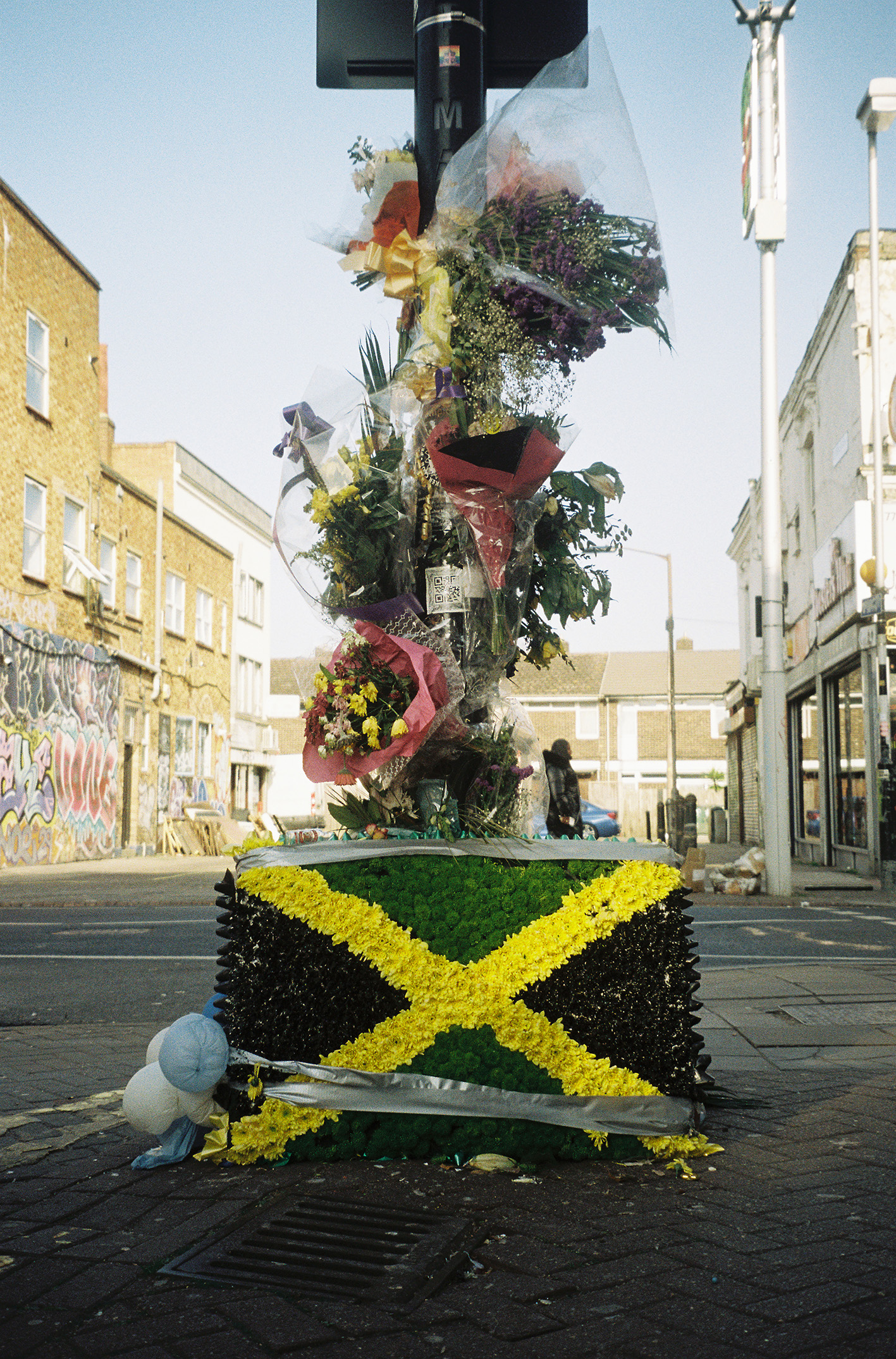 Colour photograph of bunches of flowers around a lamppost on top of a floral arrangement of the Jamaican flag