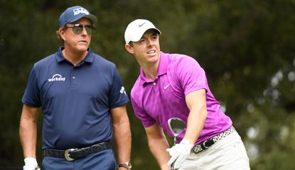 McIlroy watches his tee shot whilst Phil Mickelson watches on