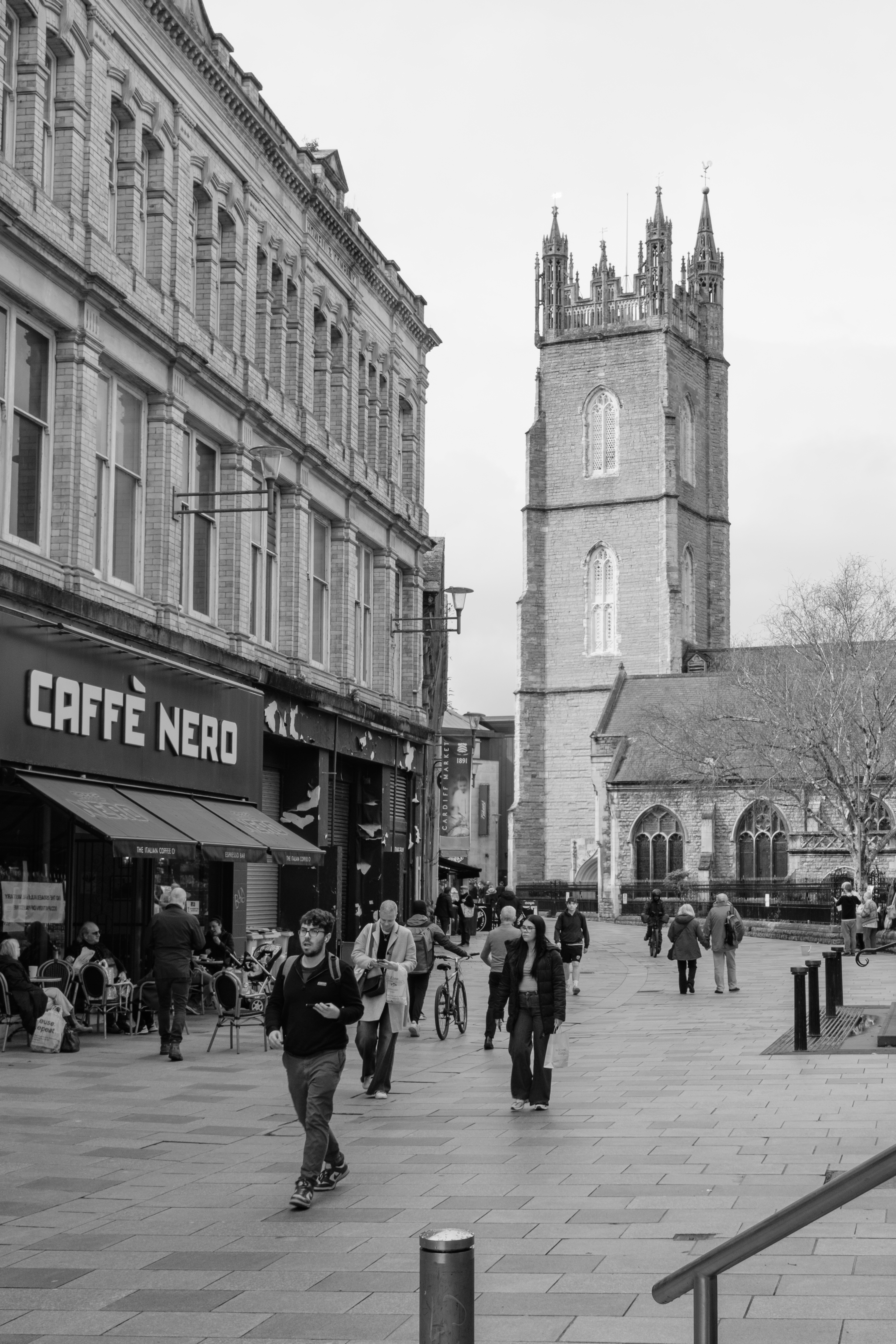 A black and white photo of The Hayes, a street in Cardiff, with a church in the background and people walking towards the camera.