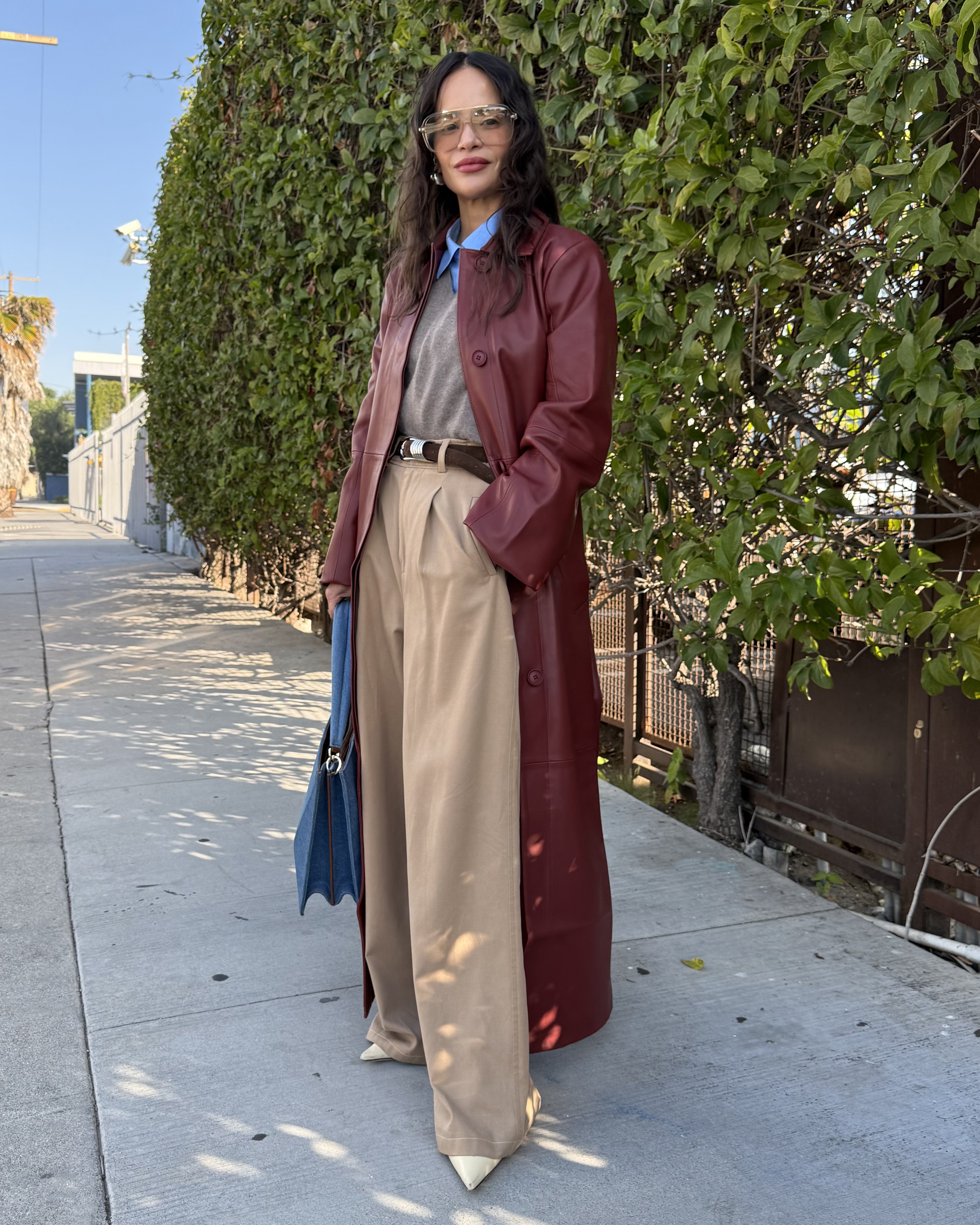 Sophie Lopez wearing a burgundy leather trench coat, a sweater, tailored trousers, and heels