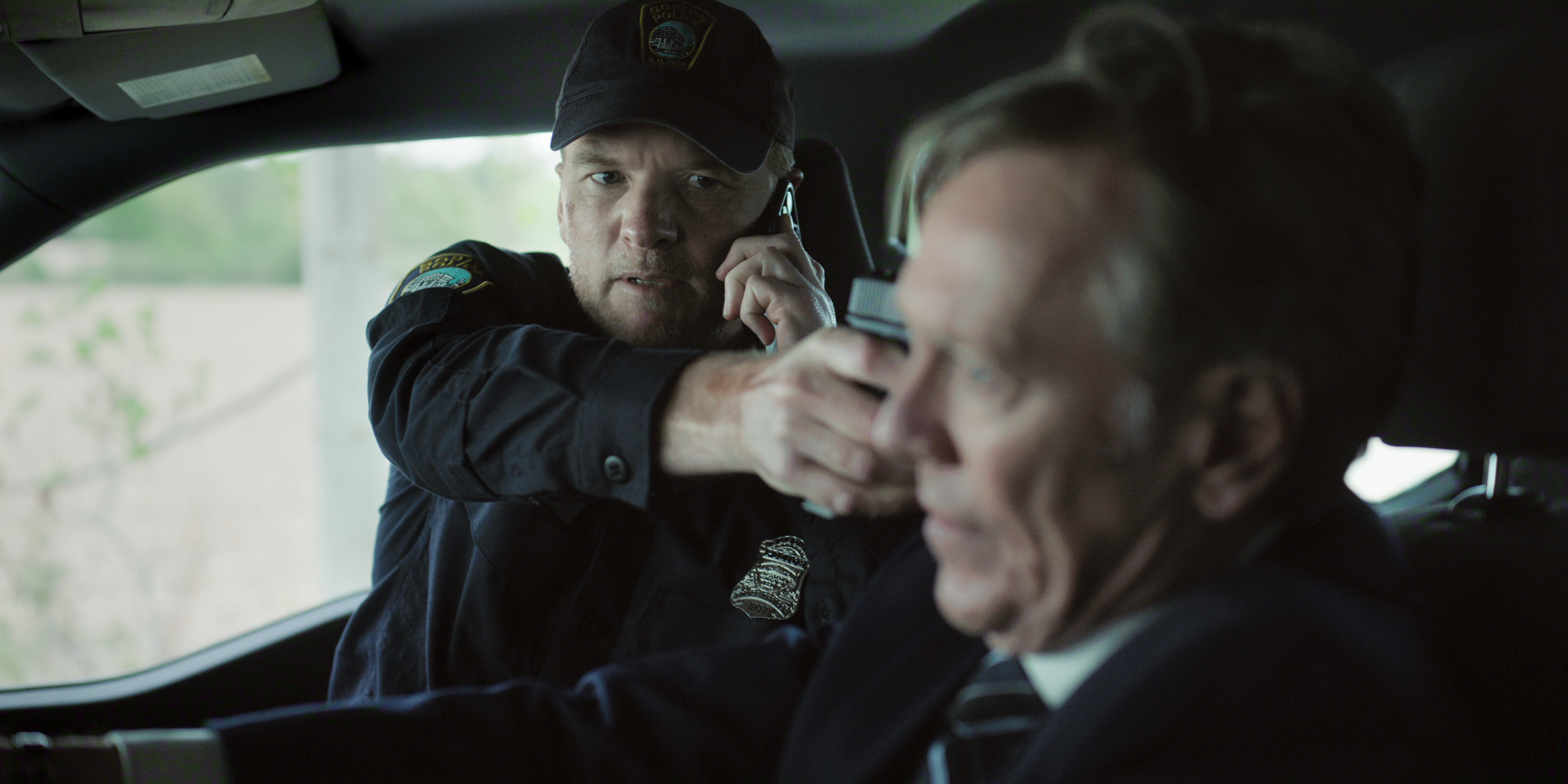 Sam Worthington as david pointing a gun in the shotgun of a car at a man in a suit driving in I Will Find You