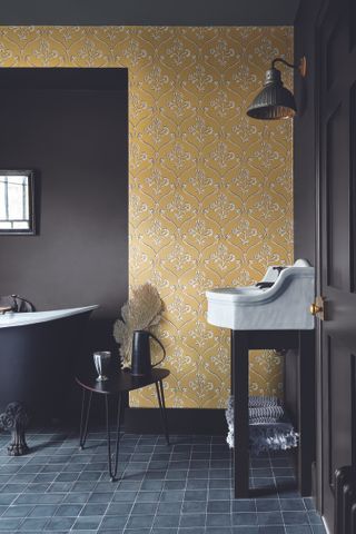 bathroom with yellow linear wallpaper design, black walls, black painted tub, black square tiles, wall light, vanity