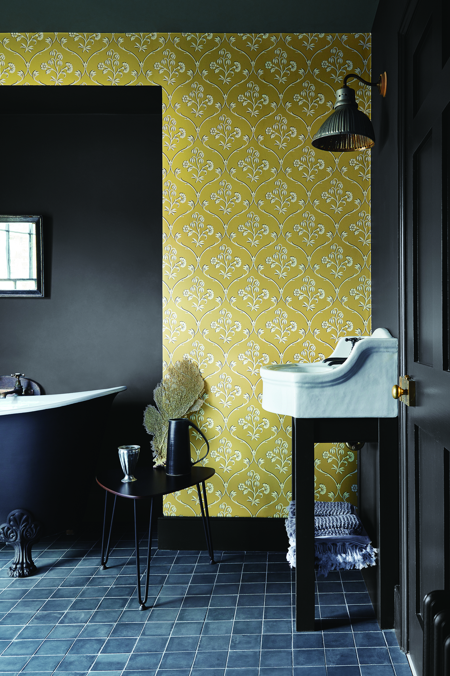 bathroom with yellow linear wallpaper design, black walls, black painted tub, black square tiles, wall light, vanity