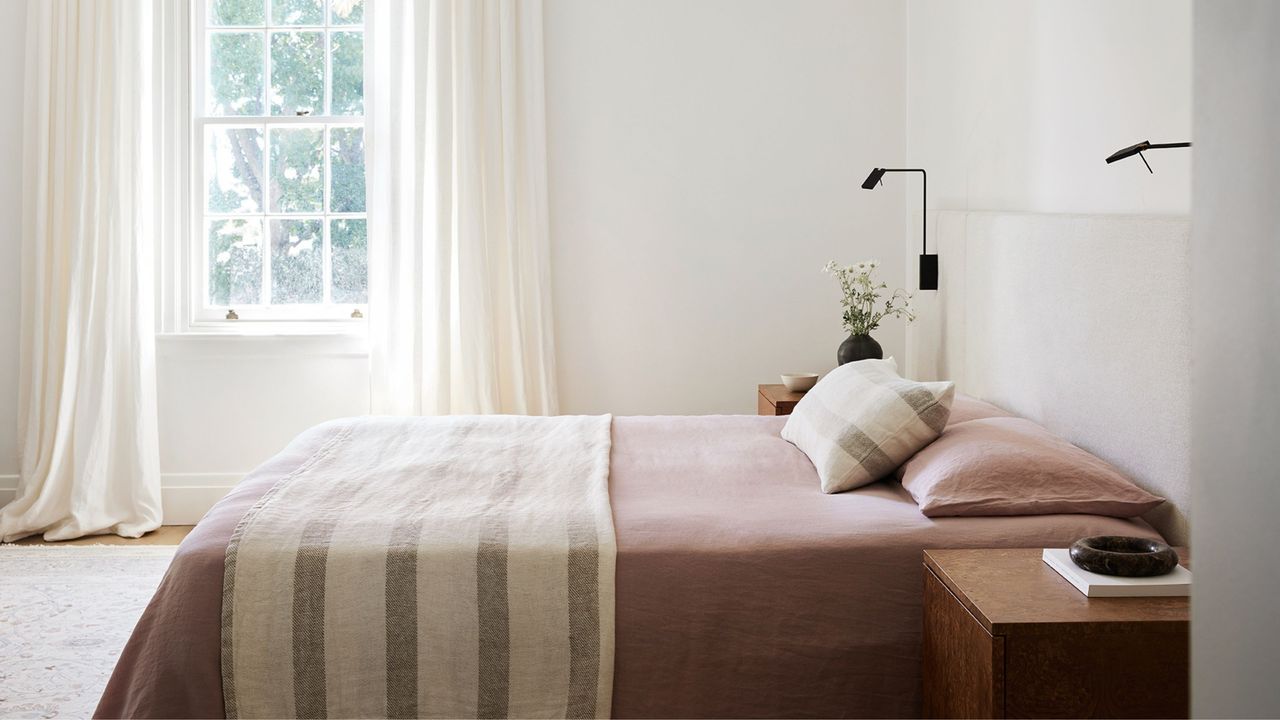 minimalist bedroom with white curtains, pink bedding and a striped throw and pillow 