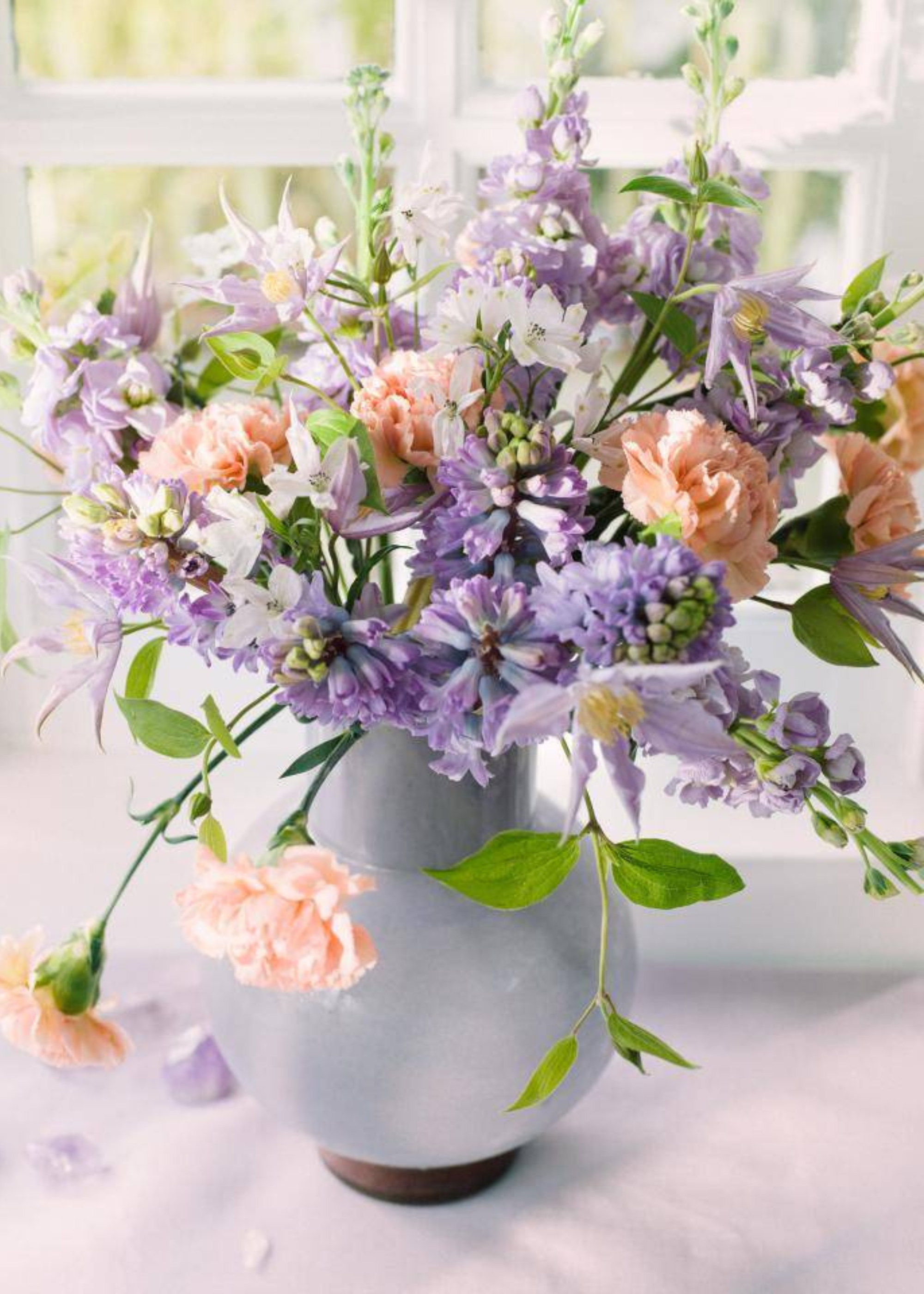 A ceramic vase with peach carnations, purple flowers and white stems