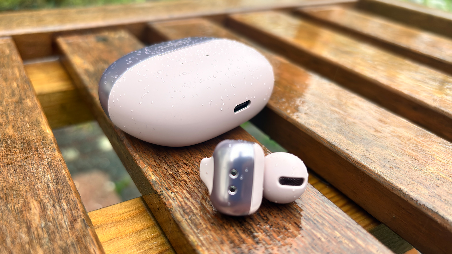 Shokz OpenDots One open earbuds on slatted wooden garden chair, one earbud next to case