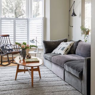 Living room with grey walls, wooden floor with grey rug and bay window with white blinds