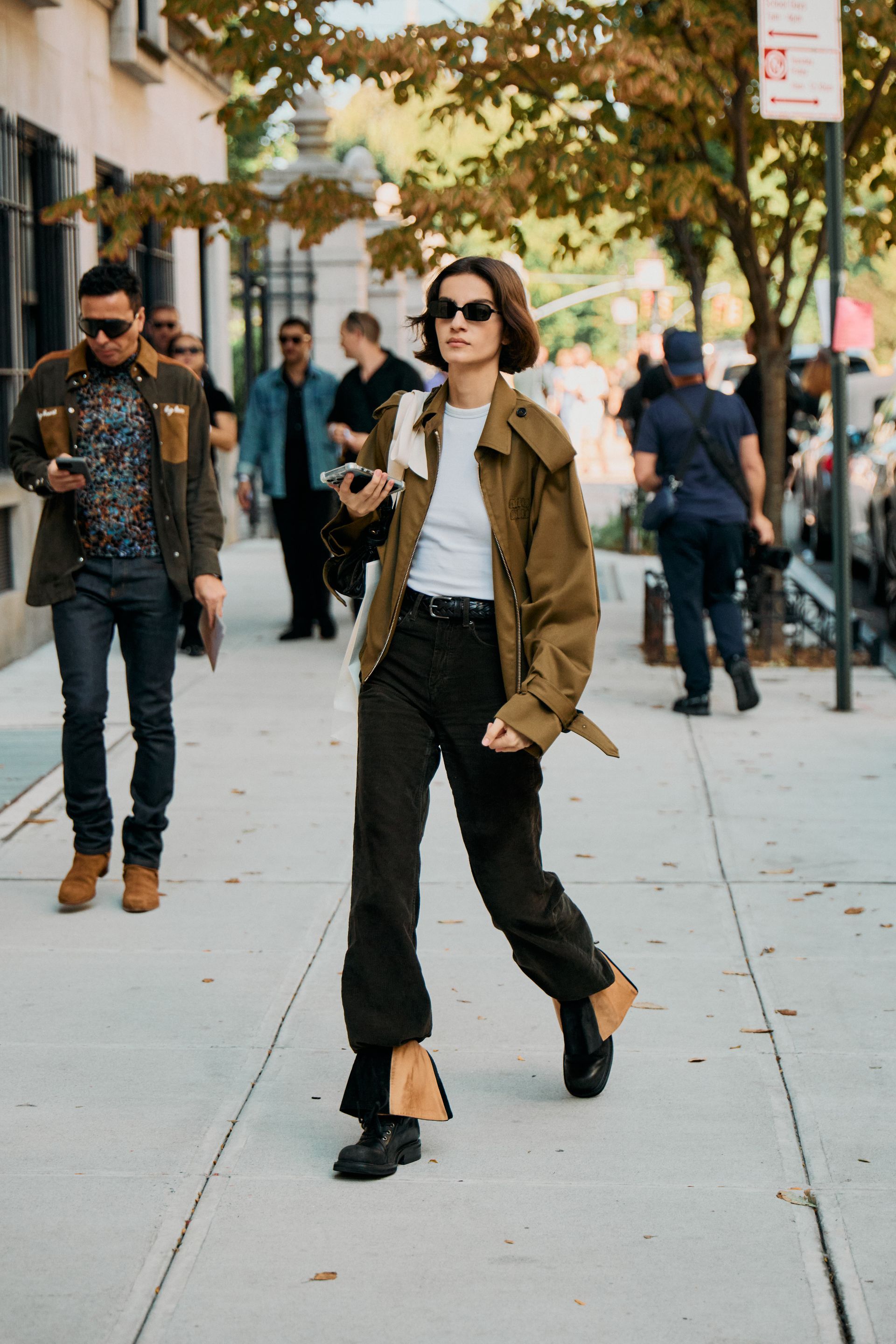 A person in a white crewneck, black jeans, and a cropped trench coat.